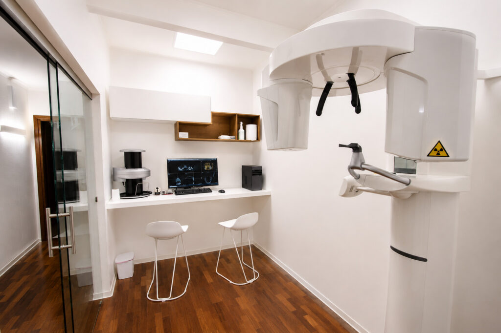 Sala con apparecchio per radiografie panoramiche, postazione con monitor e due sgabelli